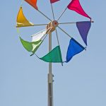 Das große Windrad Wirbelwind mit den regenbogenbunten Segeln dreht sich vor blauem Himmel