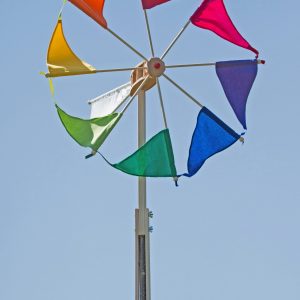 Das große Windrad Wirbelwind mit den regenbogenbunten Segeln dreht sich vor blauem Himmel