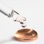 Aus einer Pipette tropft ein Tropfen auf eine Münze