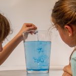 Zwei Mädchen beobachten blaue Wasserwirbel in einem Glas