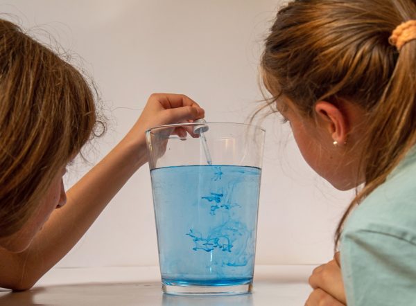 Zwei Mädchen beobachten blaue Wasserwirbel in einem Glas