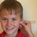 Ein Junge staunt über die Töne in seinem Ohr, die die Stimmgabel auf seinen Kopf überträgt, ein Versuch aus dem Experimentierkasten Horchkiste