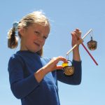 Ein Mädchen hält die kleine Balkenwaage hoch und will eine Kugel wiegen.