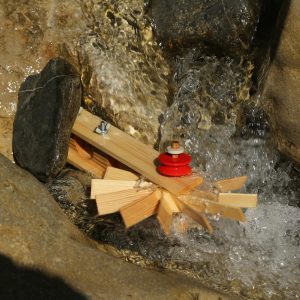 Die kleine Holzturbine dreht sich schnell im fliessenden Wasser zwischen Steinen.