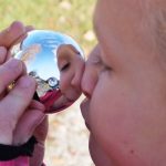 Ein Mädchen sieht ihr in der Spiegelkugel lustig verzerrtes Gesicht an.