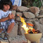 ein Junge schaut ins Feuer der Feuerschale Zwergenfeuer und macht Stockbrot
