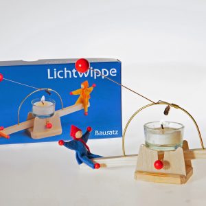 Ein rot-blaues Püppchen-Paar wippt auf der Lichtwippe vor der Produktschachtel