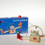 die rot-grünen Püppchen wippen auf der Lichtwippe vor der Produktschachtel